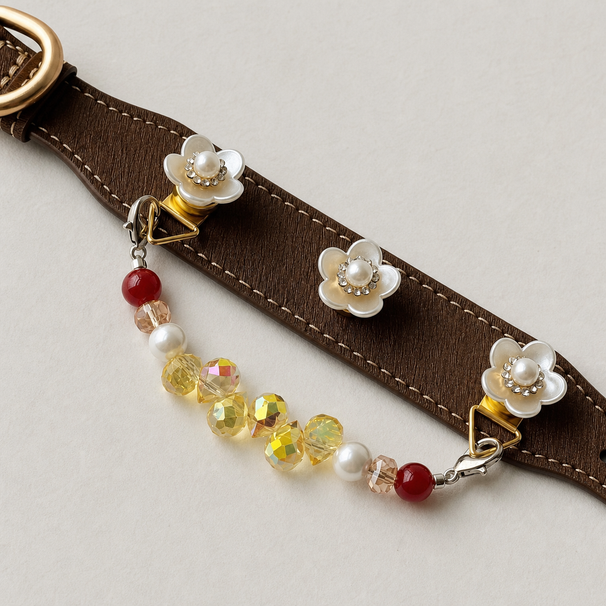 Close-up of white floral charms, contrast stitching and multicolor bead strand on brown collar