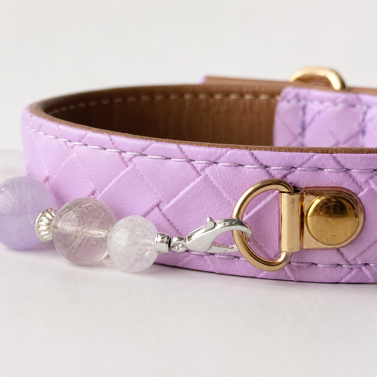 Close-up of lavender collar stitching, gold-tone ring and silver lobster clasp